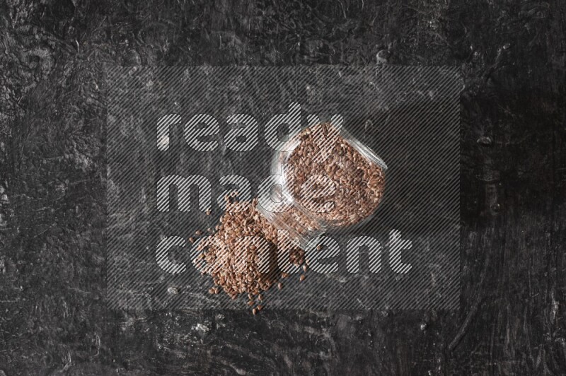 وعاء زجاجي مقلوب ممتلئ بحبوب بذر الكتان والحبوب متناثرة منه علي خلفية سوداء