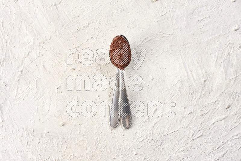 2 metal spoons full of garden cress on a textured white flooring in different angles