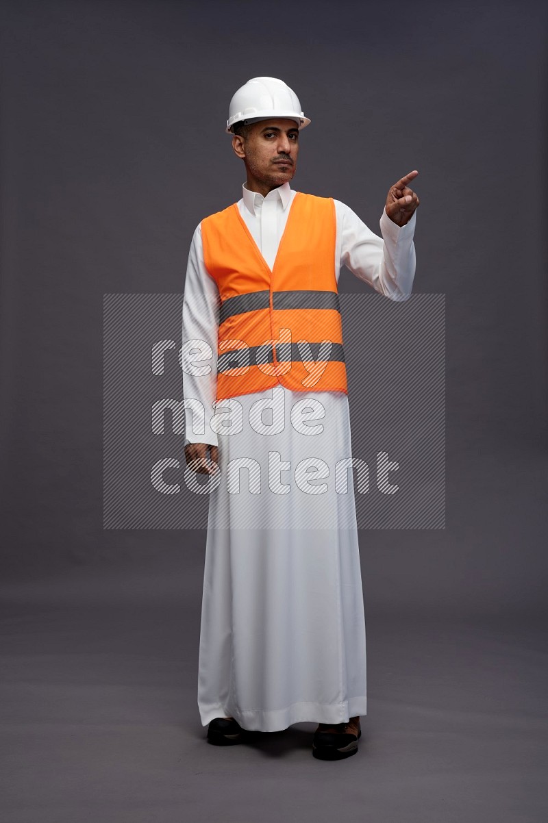 Saudi man wearing thob with engineer vest standing interacting with the camera on gray background