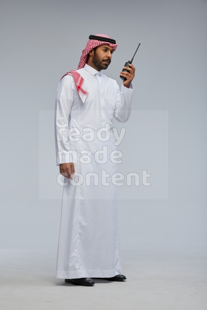 Saudi man Wearing Thob and shomag standing holding walkie-talkie on Gray background