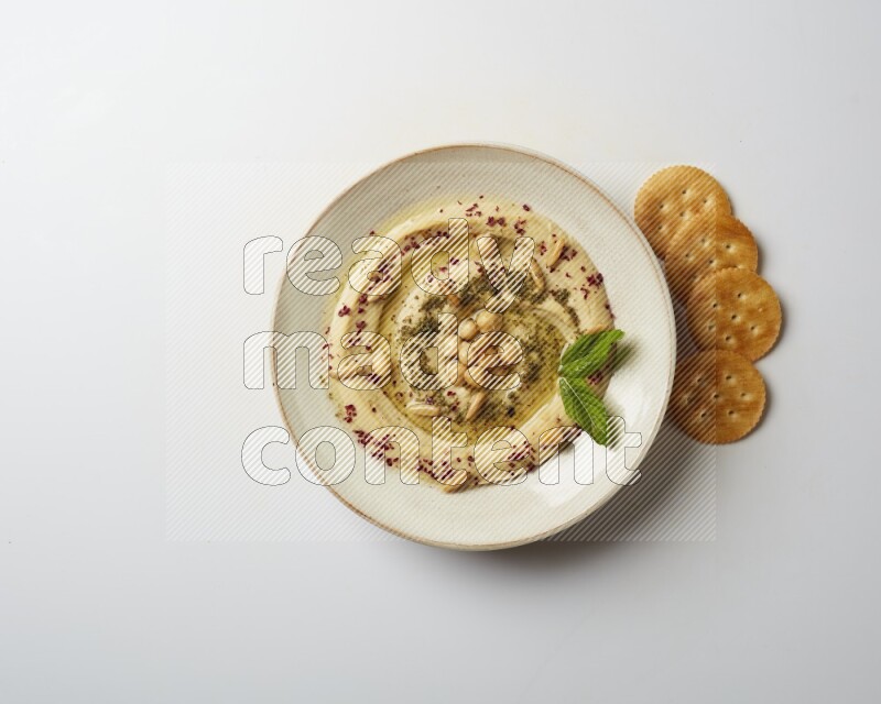Hummus in a pottry plate garnished with zaatr & sumak on a white background