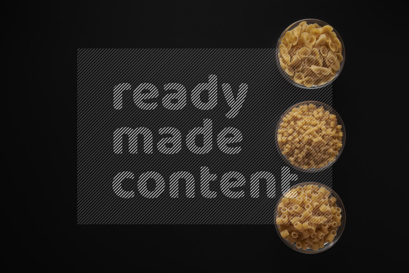 Different pasta types in 3 glass bowls on black background