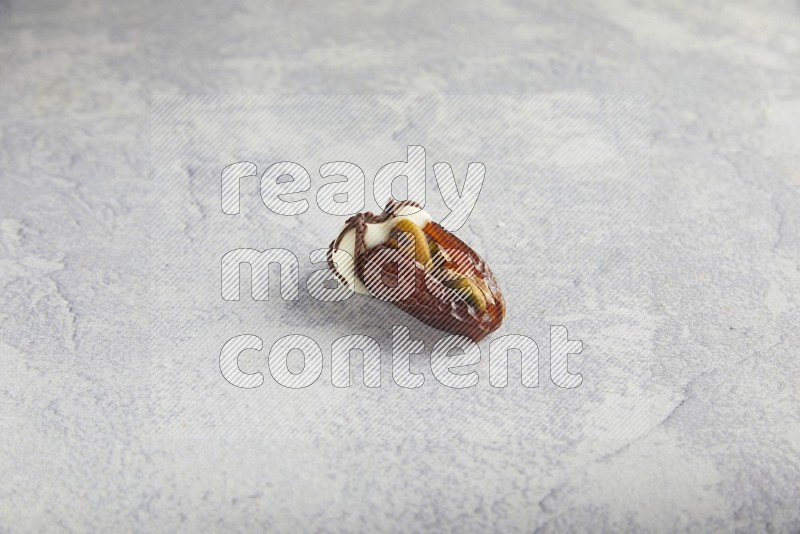 pistachio stuffed date covered with white chocolate with dark chocolate drizzle on a light grey background