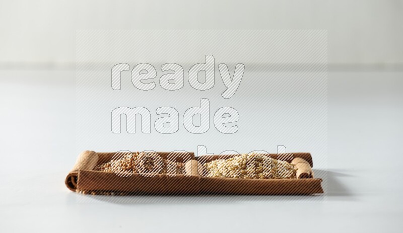 مربعان من أعواد القرفة ممتلئان بحبوب الخردل وبذور السمسم علي خلفية بيضاء