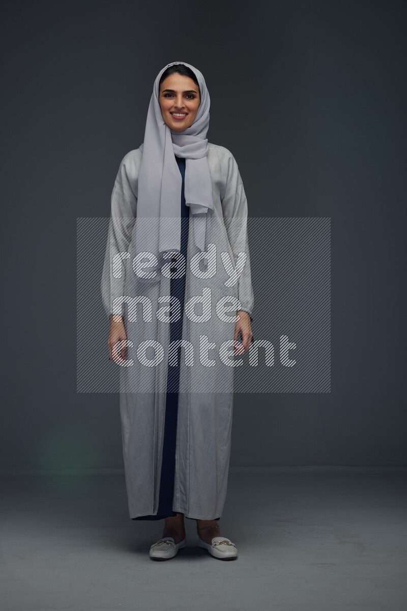 A Saudi woman wearing a light gray Abaya and head scarf standing and making multi poses eye level on a grey background