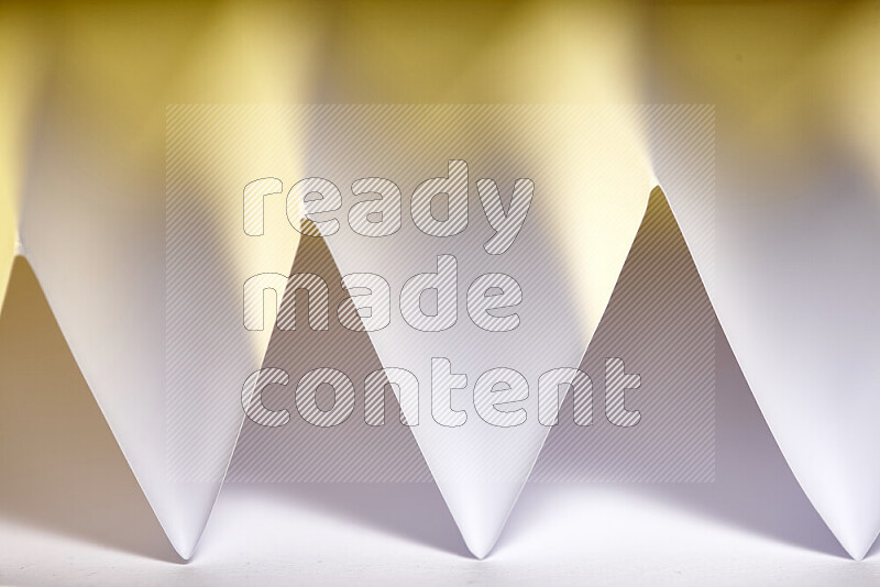 A close-up abstract image showing sharp geometric paper folds in white gradients and warm tones