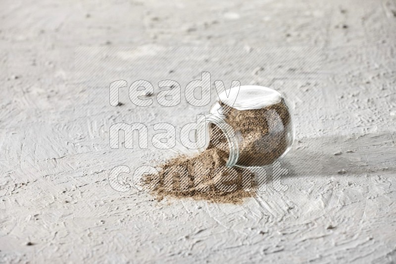 Flipped glass spice jar full of black pepper powder on a textured white flooring