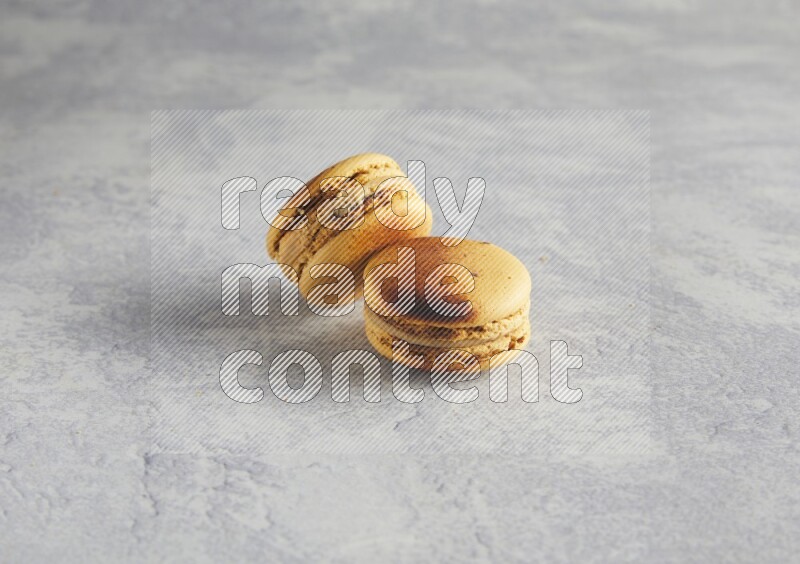 45º Shot of two Yellow Crème Brulée macarons on white  marble background