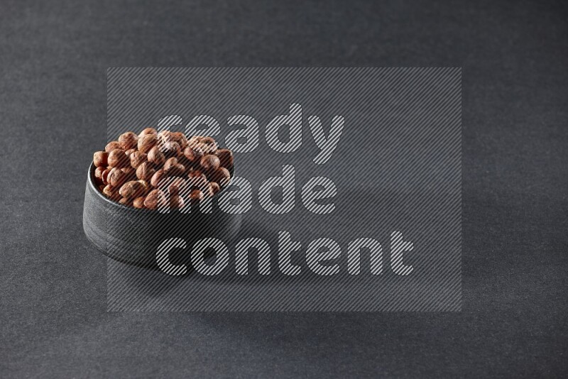 A black pottery bowl full of peeled hazelnuts on a black background in different angles