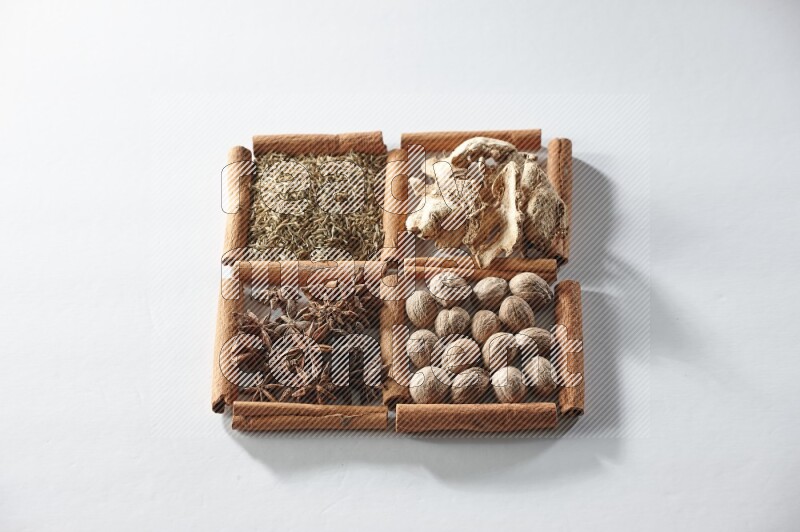 4 مربعات من أعواد القرفة ممتلئة باليانسون والزنجبيل والكمون وجوزة الطيب على أرضية بيضاء