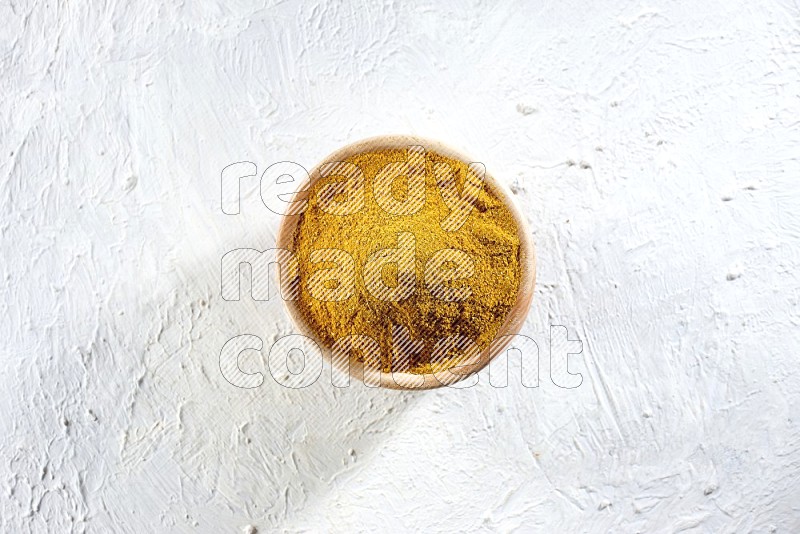 A wooden bowl full of turmeric powder on a textured white flooring