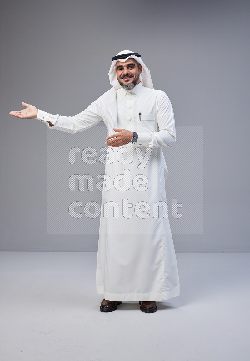 Saudi man Wearing Thob and white Shomag standing interacting with the camera on Gray background