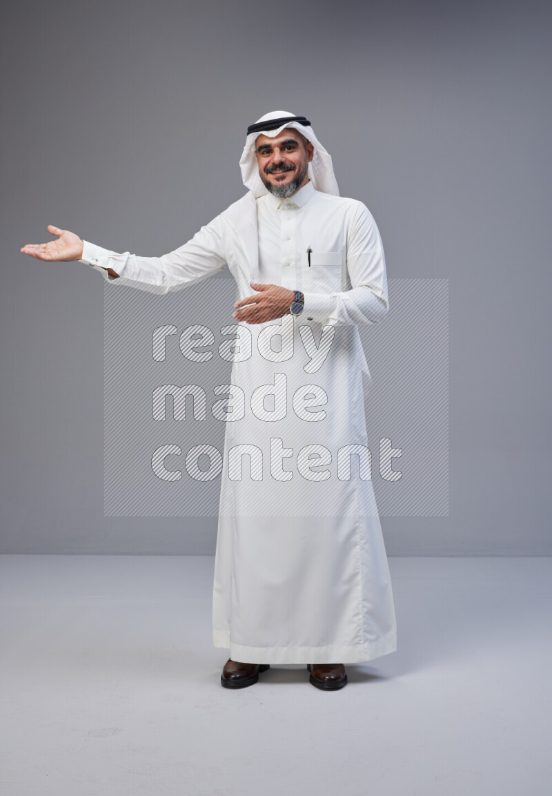 Saudi man Wearing Thob and white Shomag standing interacting with the camera on Gray background