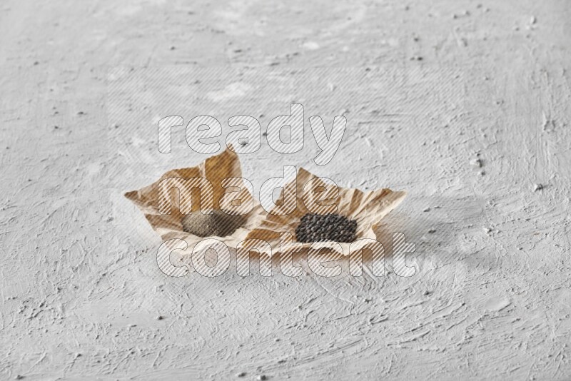 Black pepper and black pepper powder on 2 crumpled pieces of craft paper on a textured white flooring