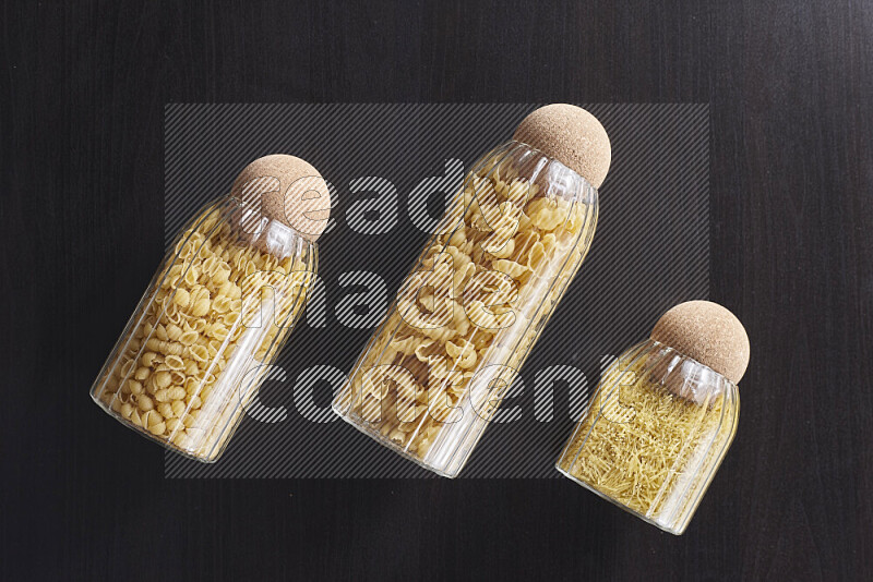 Raw pasta in glass jars on black background