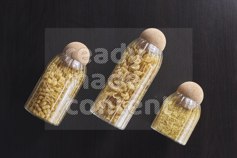 Raw pasta in glass jars on black background