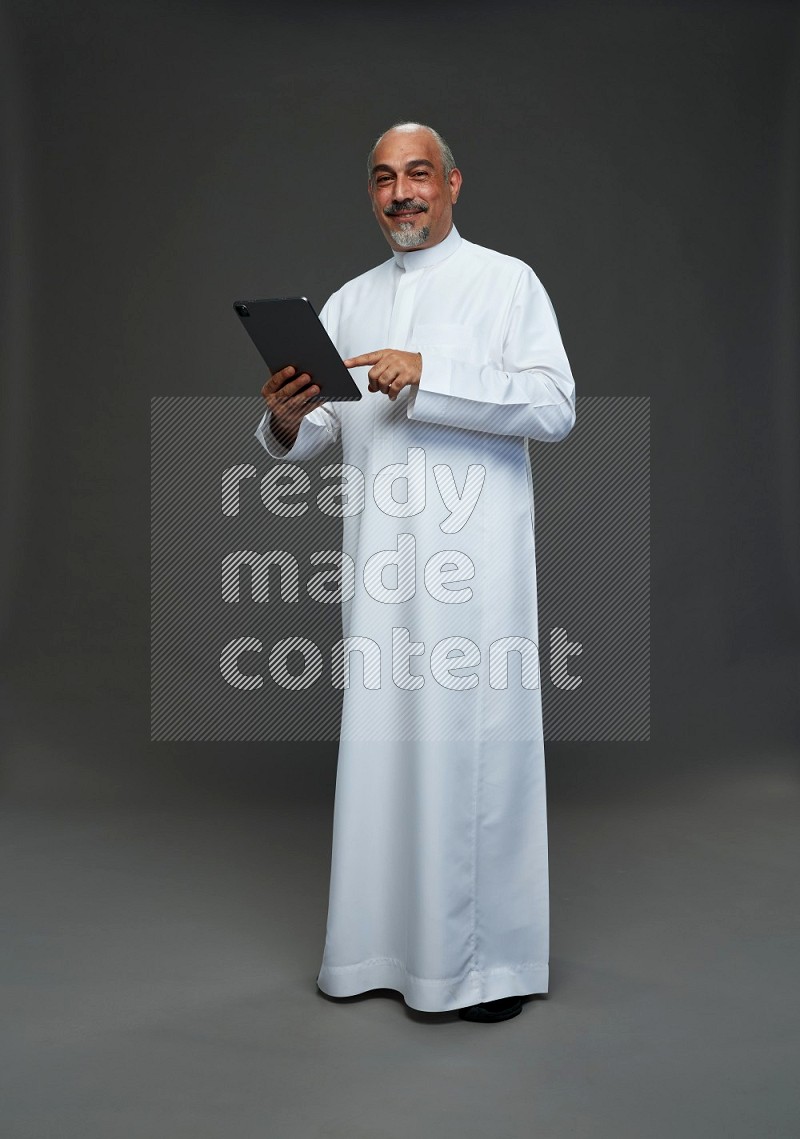 Saudi man without shomag Standing working on tablet on gray background