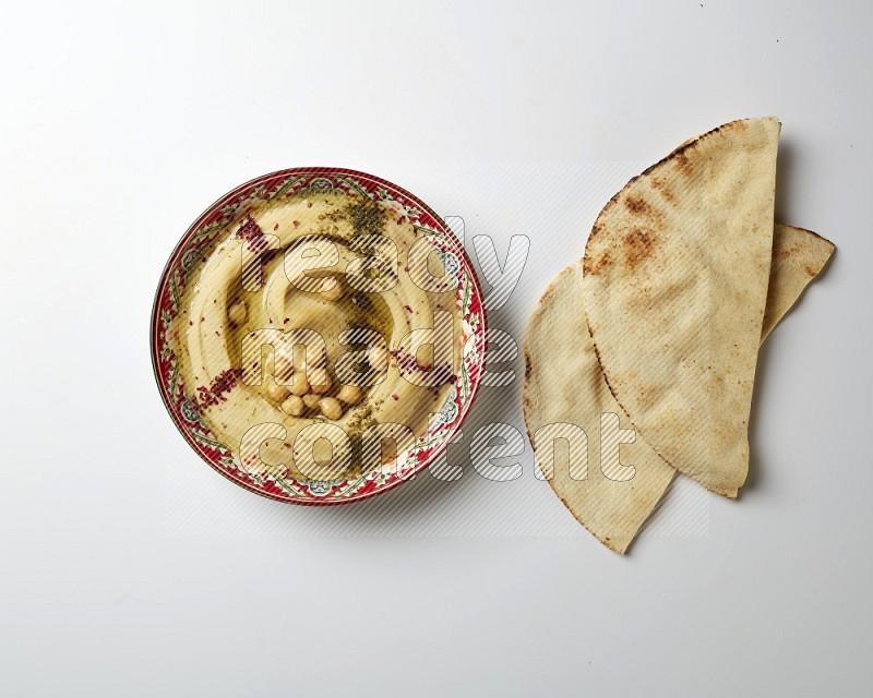 Hummus in a red plate with patterns garnished with zaatar & sumak on a white background