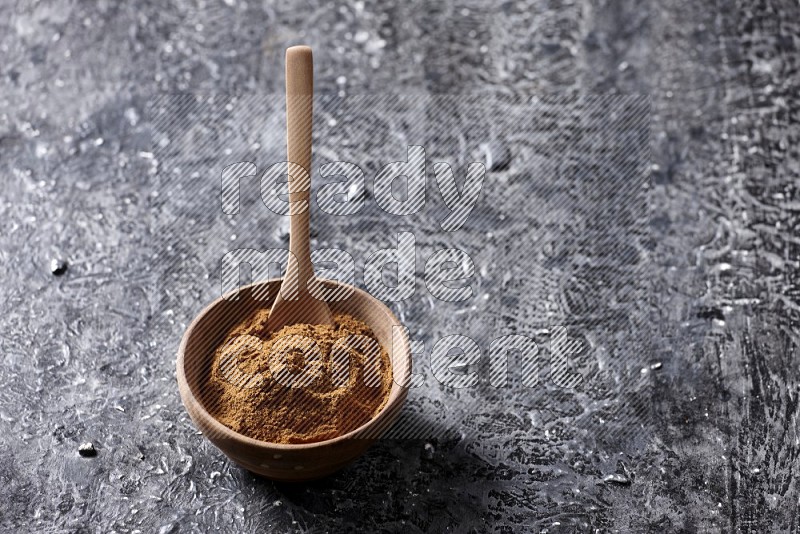 Wooden bowl full of cinnamon powder with a wooden spoon on a textured black background in different angles