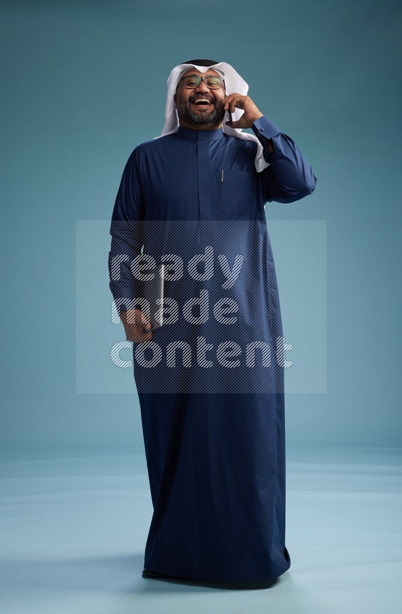 Saudi Man with shimag Standing talking on phone on blue background