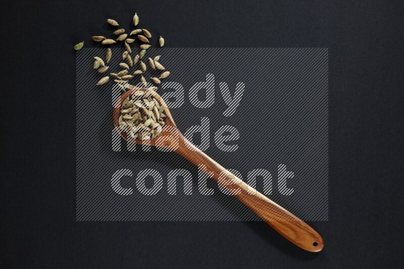 A wooden ladle full of cardamom on black flooring