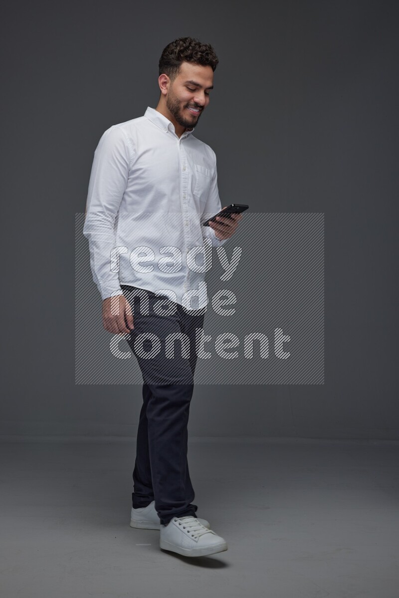 A man wearing smart casual standing and using his phone eye level on a gray background