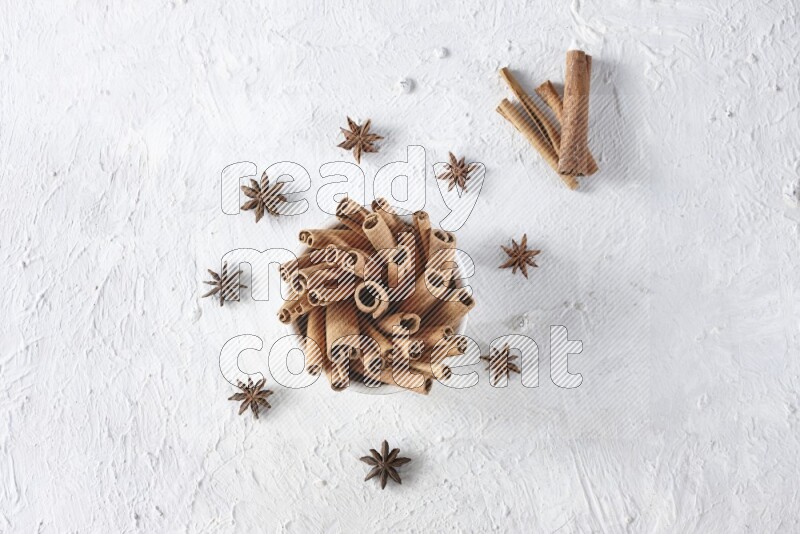 White bowl full of cinnamon sticks surrounded by star anis on a textured white background in different angles