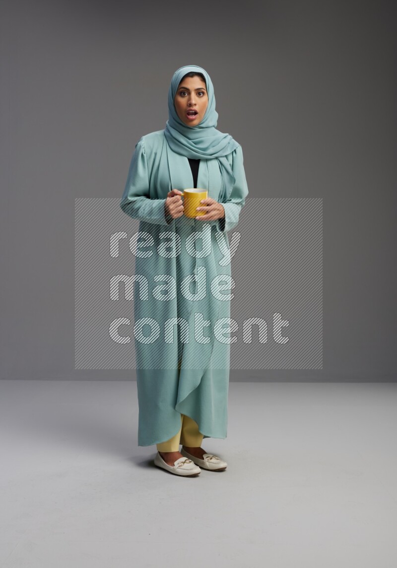 Saudi Woman wearing Abaya standing  holding a mug on Gray background