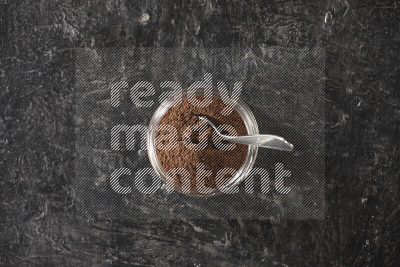 وعاء زجاجي ممتلئ ببودرة القرنفل مع ملعقة معدنية على أرضية سوداء