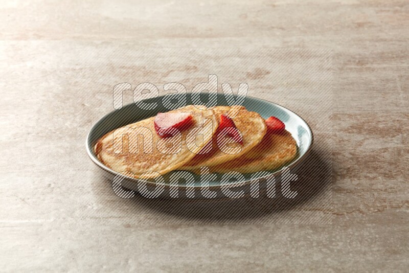 Three stacked strawberry pancakes in a blue plate on beige background