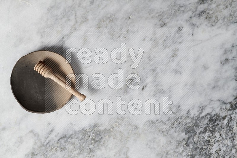 Multicolored Pottery Plate with wooden honey handle in it, on grey marble flooring, Top View