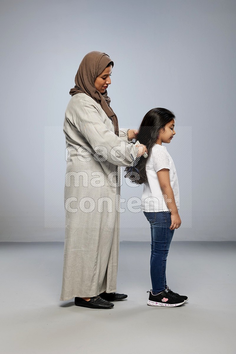 Mom standing styling hair for her daughter on gray background