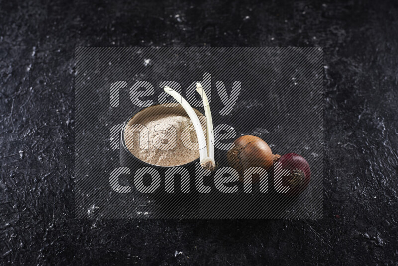 A black pottery bowl full of onion powder on black background