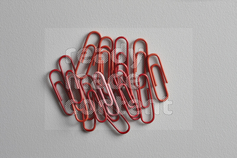 A bunch of red paper clips with a different colored paper clip in the center on grey background