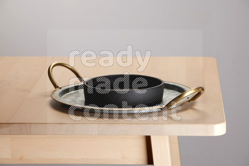 black bowl placed on a rounded stainless steel tray with golden handels on the edge of wooden table