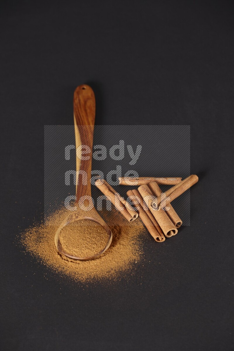 Cinnamon powder in a spoon ladle and spreaded on the floor beside it cinnamon sticks on the floor on black background in different angles