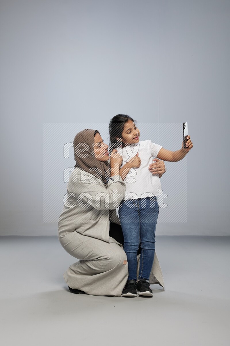 A girl standing taking selfie with her mother on gray background