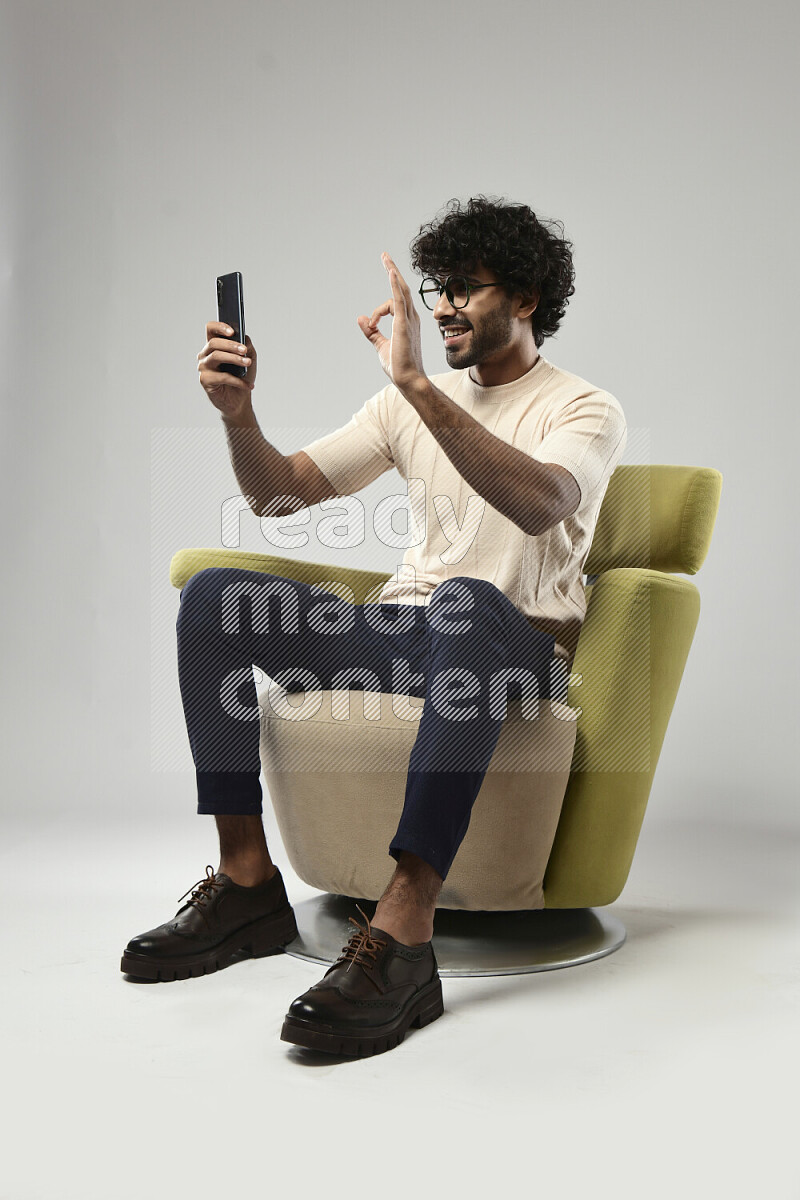 A man wearing casual sitting on a chair shooting with his phone on white background