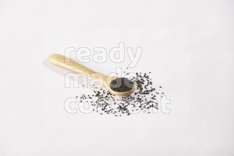 A wooden spoon full of black seeds on a white flooring