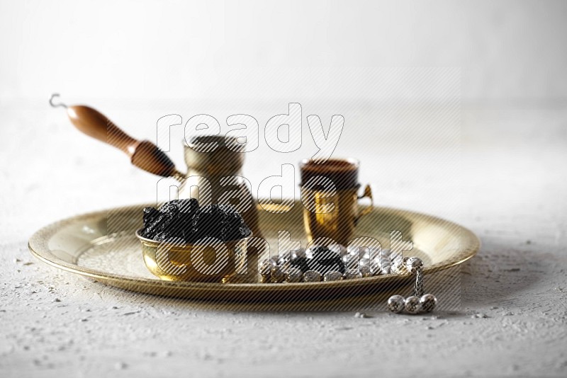 Dried plums in a metal bowl with coffee and prayer beads on a tray in a light setup