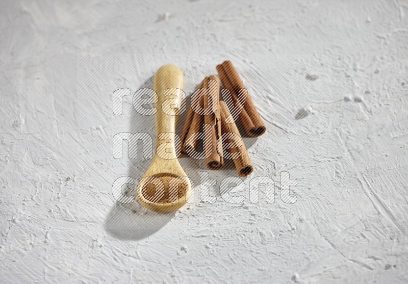 Cinnamon powder in a wooden spoon with cinnamon sticks on white background