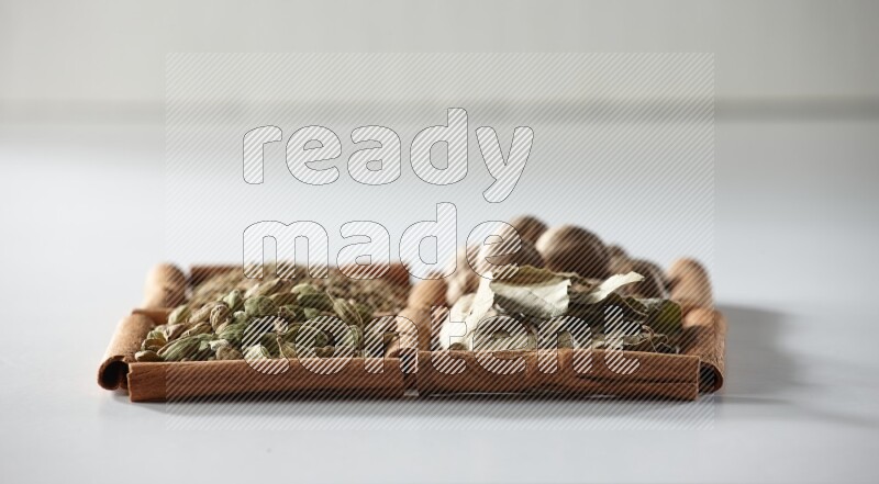 4 مربعات من أعواد القرفة ممتلئة بجوزة الطيب وأوراق الغار وحبوب الهيل والكمون على أرضية بيضاء