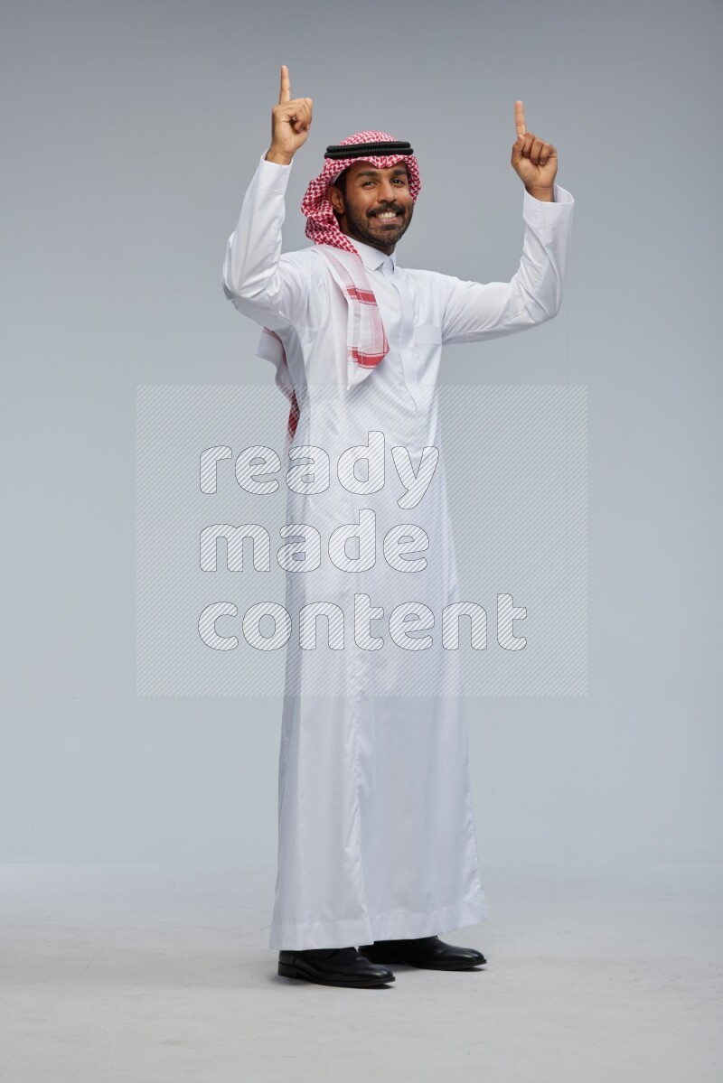Saudi man Wearing Thob and shomag standing interacting with the camera on Gray background