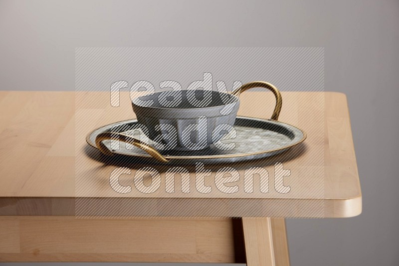 grey bowl placed on a rounded stainless steel tray with golden handels on the edge of wooden table