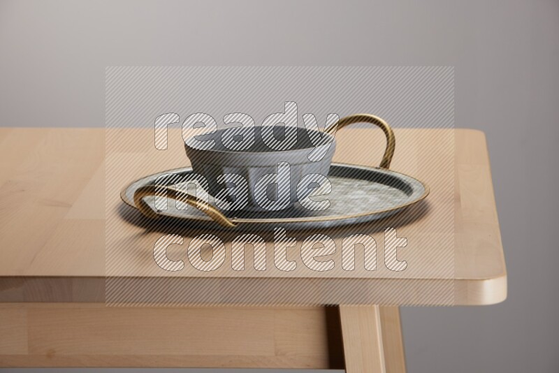 grey bowl placed on a rounded stainless steel tray with golden handels on the edge of wooden table