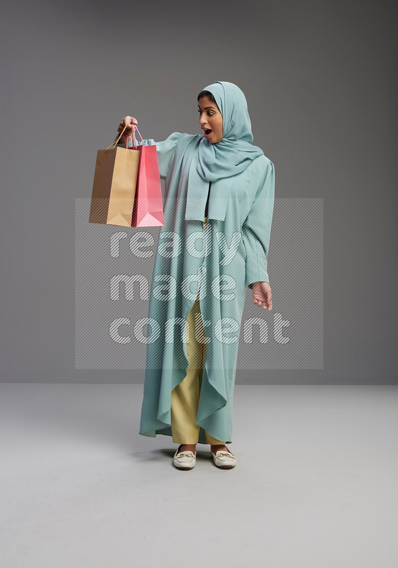 Saudi Woman wearing Abaya standing holding shopping bag on Gray background