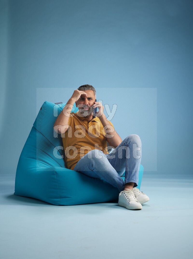 A man sitting on a blue beanbag and talking on the phone