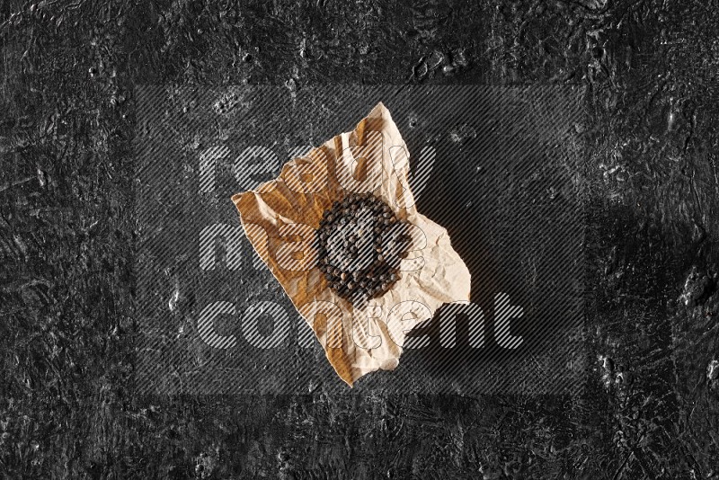 Black pepper beads on crumpled paper on a textured black flooring