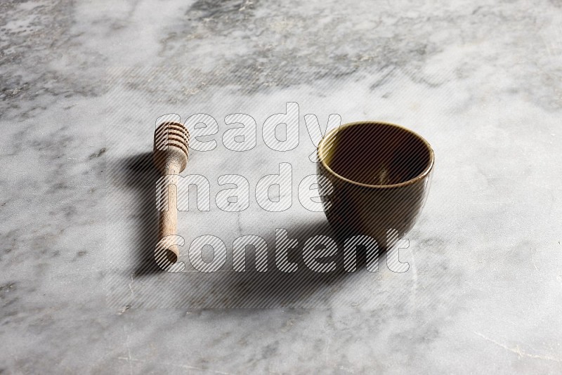 Multicolored Pottery cup with wooden honey handle on the side with grey marble flooring, 45 degree angle