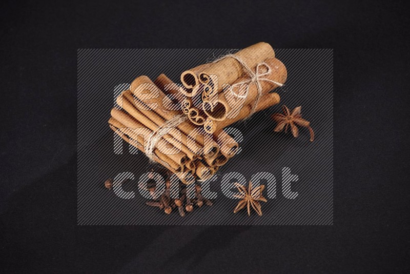 Two bounded stacks of cinnamon sticks with cloves and star anise on black background